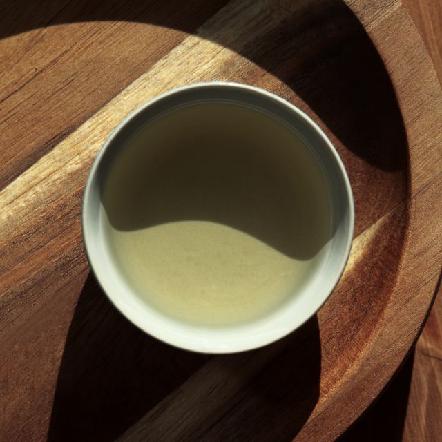 Stark sol lyser in på en tekopp som står på träbord, vilket skapar hårda skuggor.