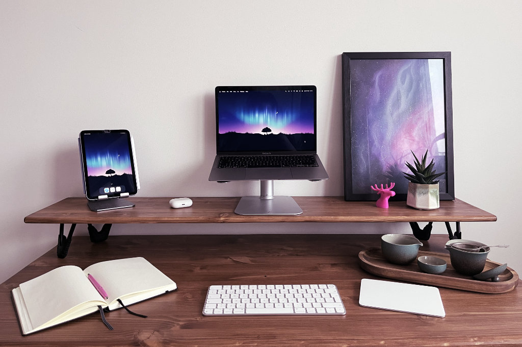 Ett lågt krivbord i trä med teknikprylar inklusive en MacBook Air, en iPad mini, ett magic keyboard, en magic trackpad och ett par AirPods Pro